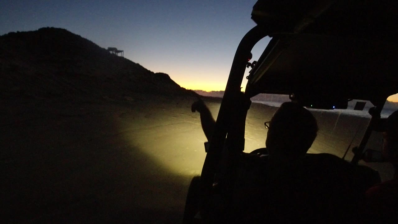 In Los Cabos, the golf cart interior frames a headlight beam on the road while a rider remains in silhouette against the dusk sky.