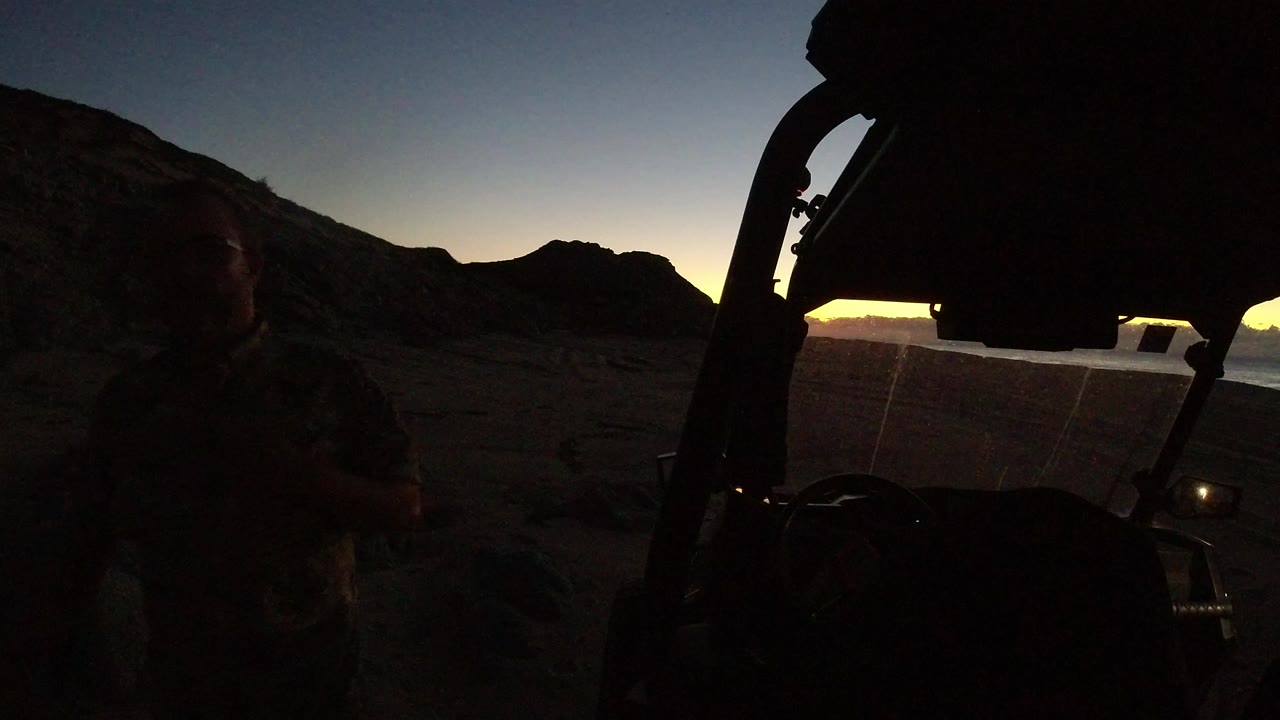 Dark Wrangler silhouette beside rocky hills at sunset.