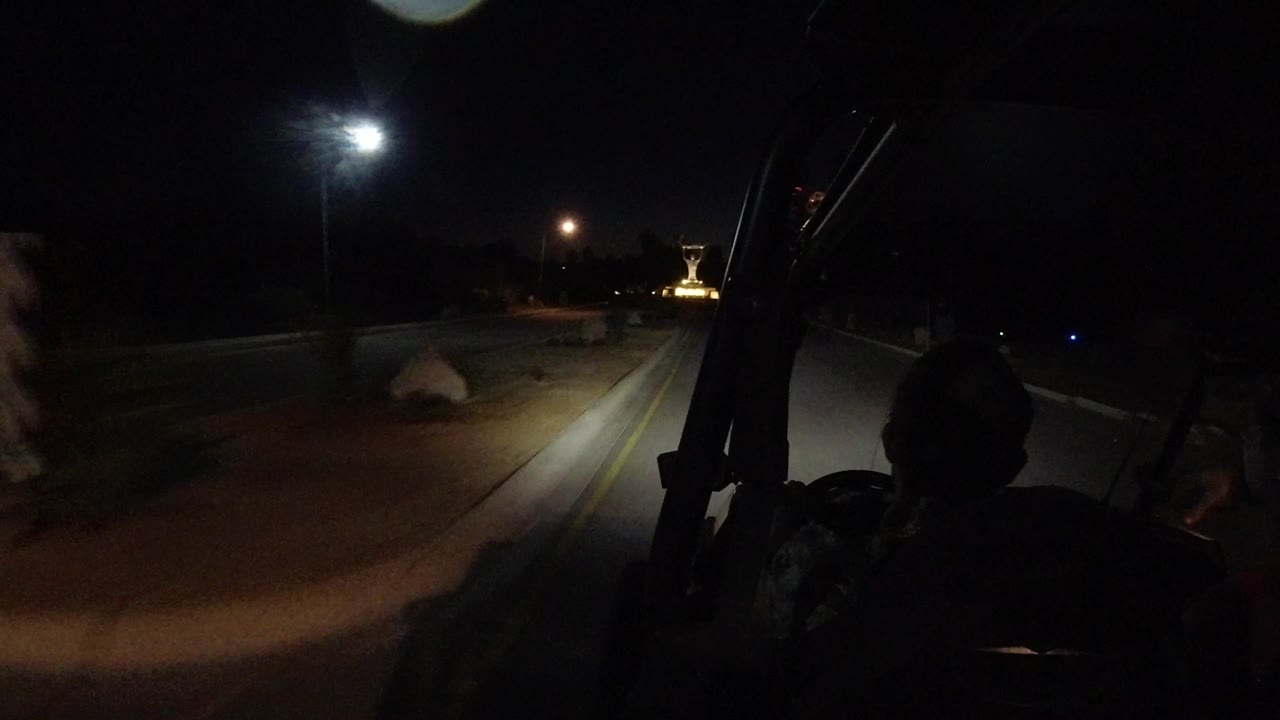 Night road seen past silhouetted riders in an open vehicle.