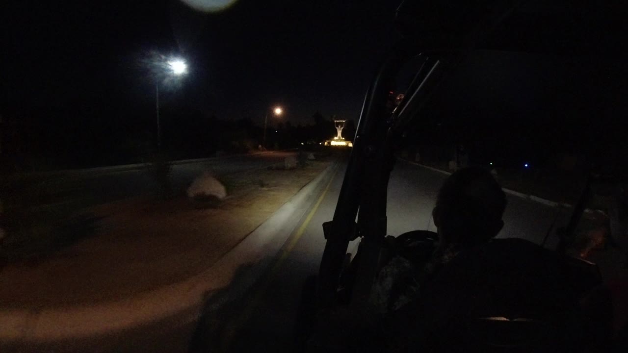 The Los Cabos road remains mostly dark as silhouetted passengers frame the foreground and a streetlamp casts light across the curb and pavement.