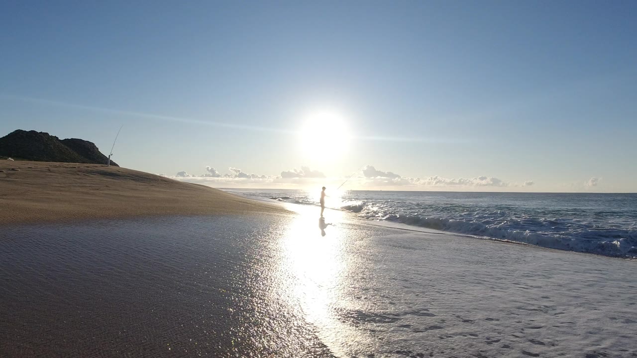 Lone person standing at the surf line under bright sun glare.