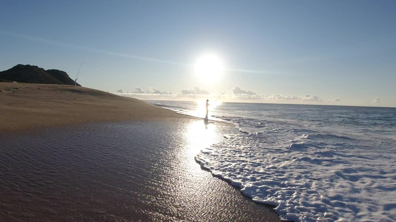 Sunrise over a beach with surf, wet sand, and a dark headland.