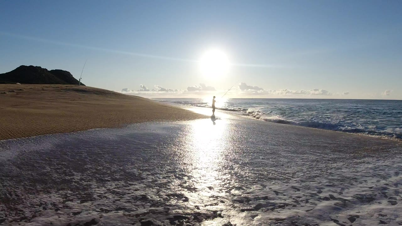 Wide beach view with a woman near the surf and bright sun reflection on wet sand.