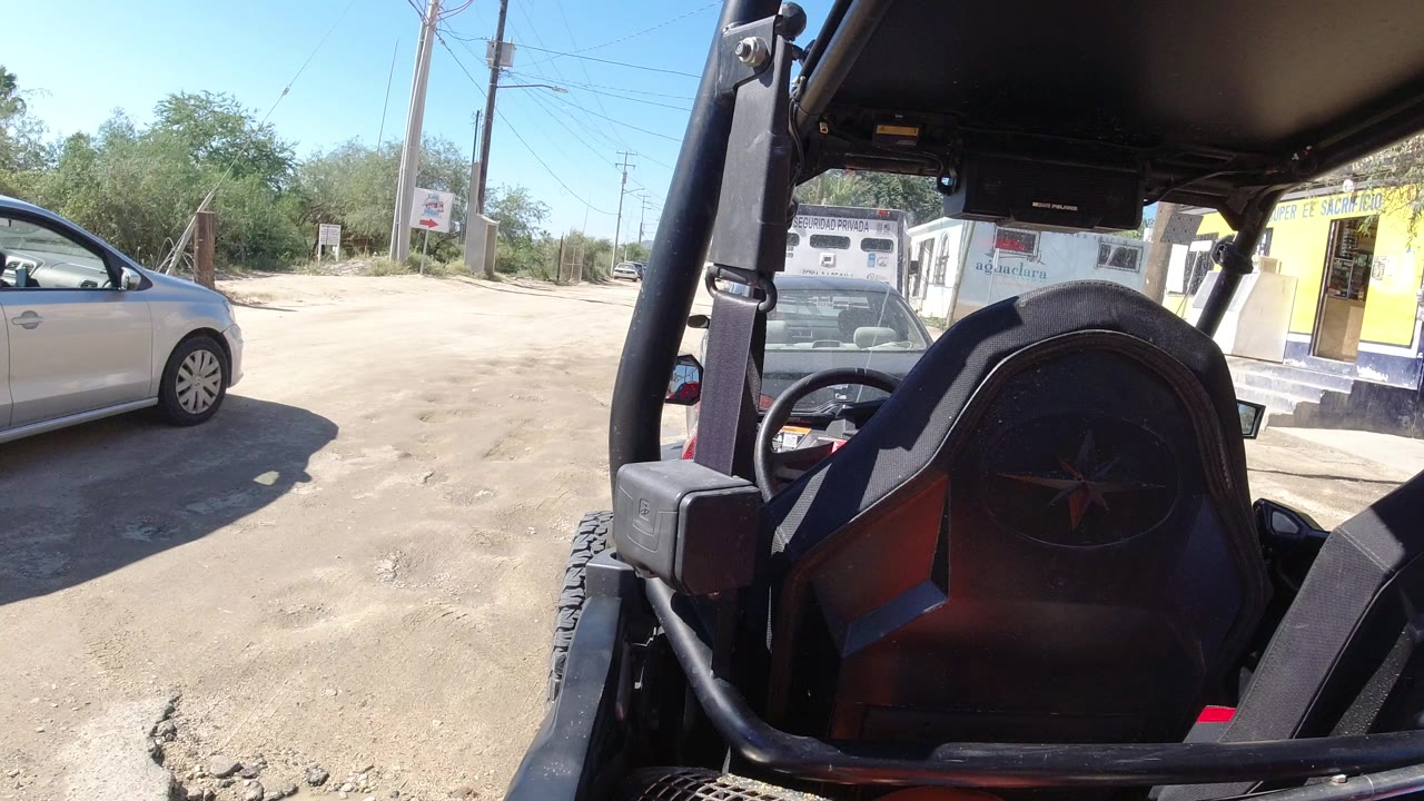Silver car passing beside a machine on a dusty roadside.