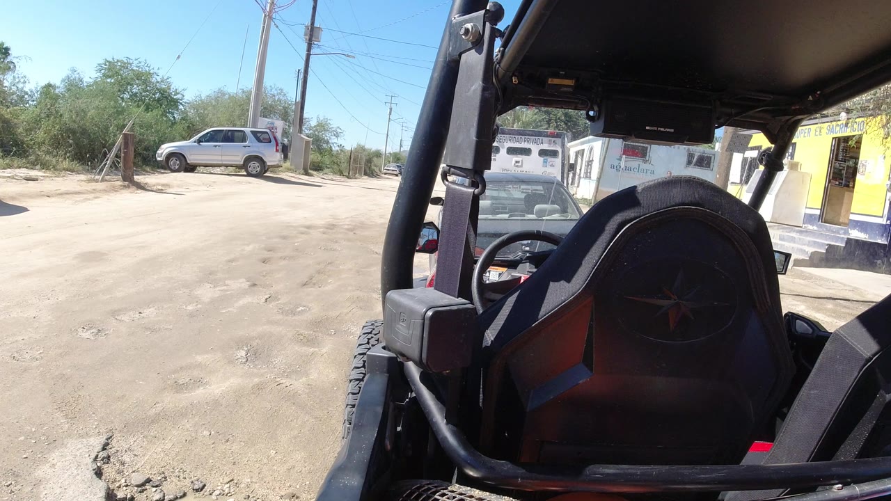 Open off-road vehicle interior facing a dusty roadside lot and parked SUV.