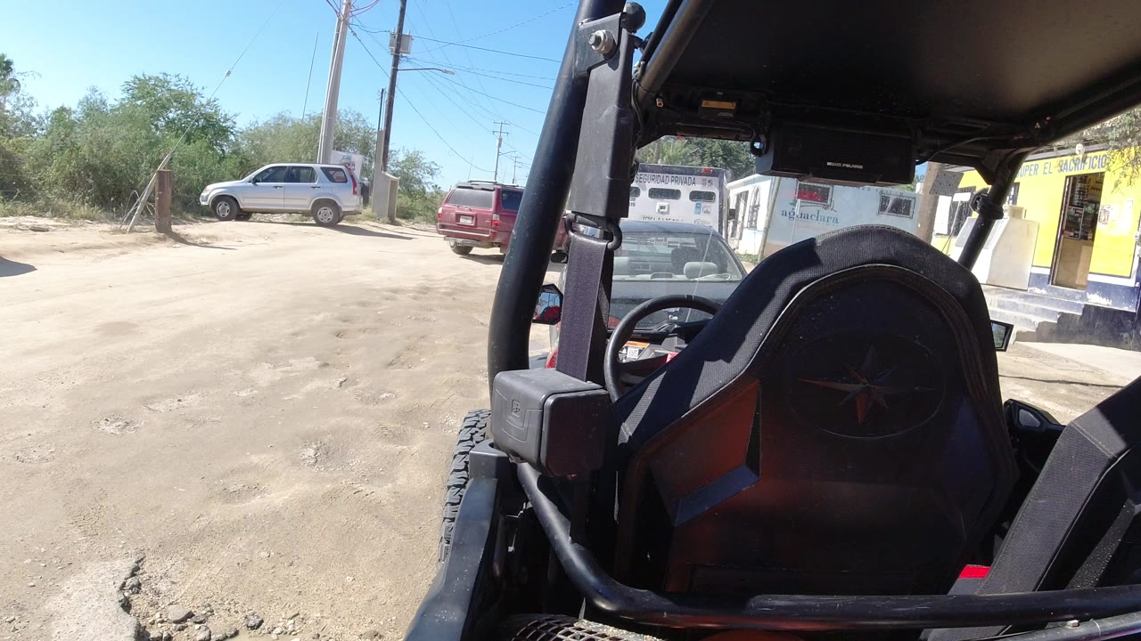 Open vehicle seat beside a dusty road and small buildings