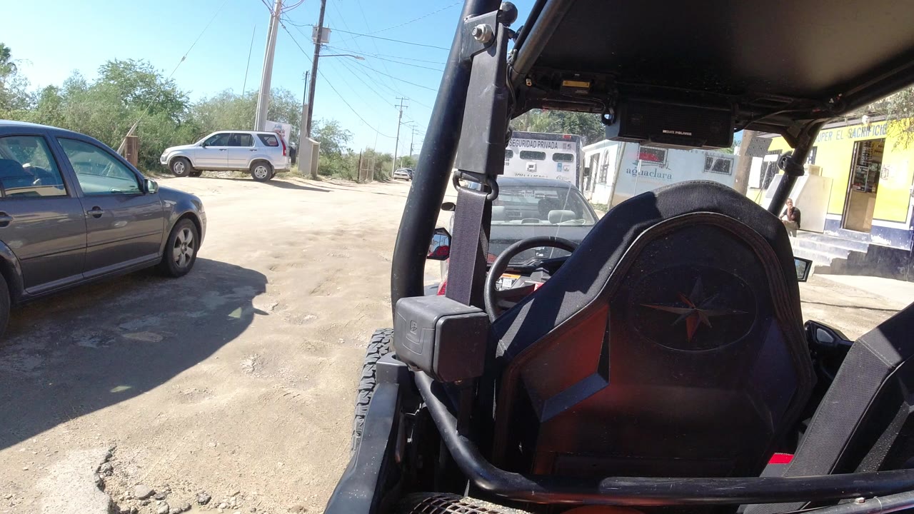 At the start of the Los Cabos clip, a gray sedan sits near the left edge while the Wrangler seat, roll bar, and roof frame the right side, with no visible people.