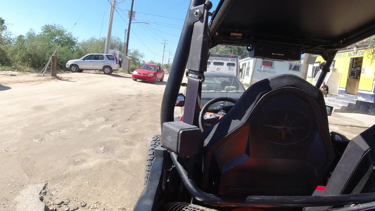 ATV seat and roll cage beside a dusty roadside lot with parked cars