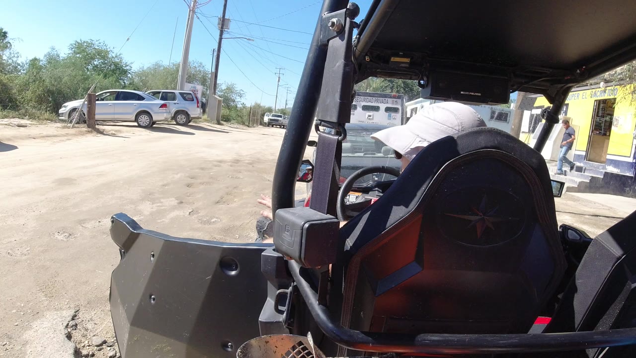 Rear seat of an open vehicle facing a sandy parking lot and yellow storefront.