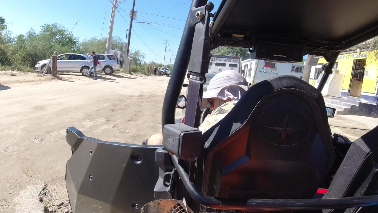 Open vehicle interior beside a dusty parking lot with parked cars and a storefront.