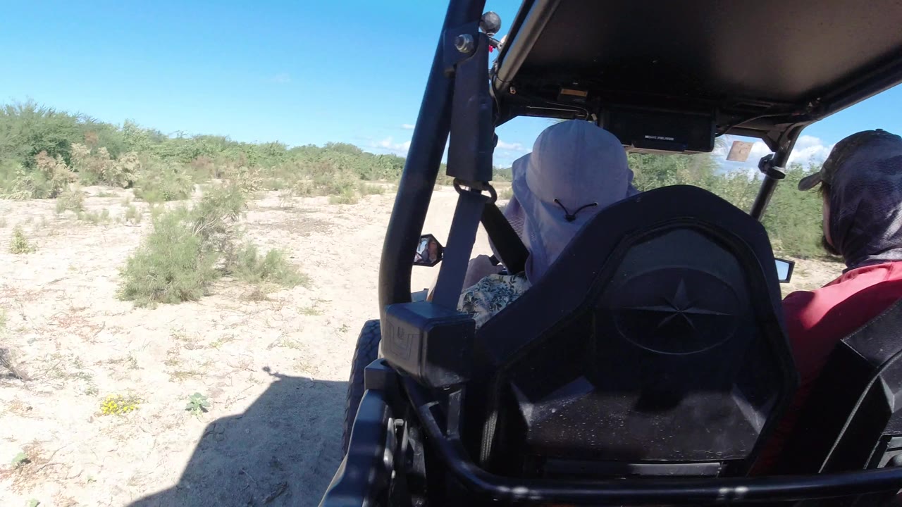 Vehicle interior beside sandy scrubland and distant hills.
