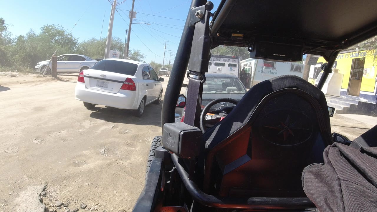 White sedan farther across a sandy roadside area with open vehicle framing.