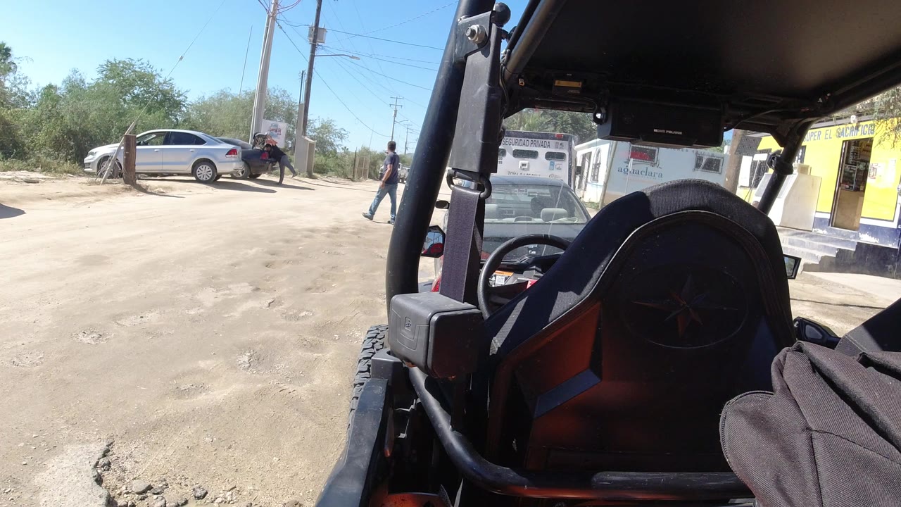 View from an open vehicle toward a dusty parking lot with a silver car and people.