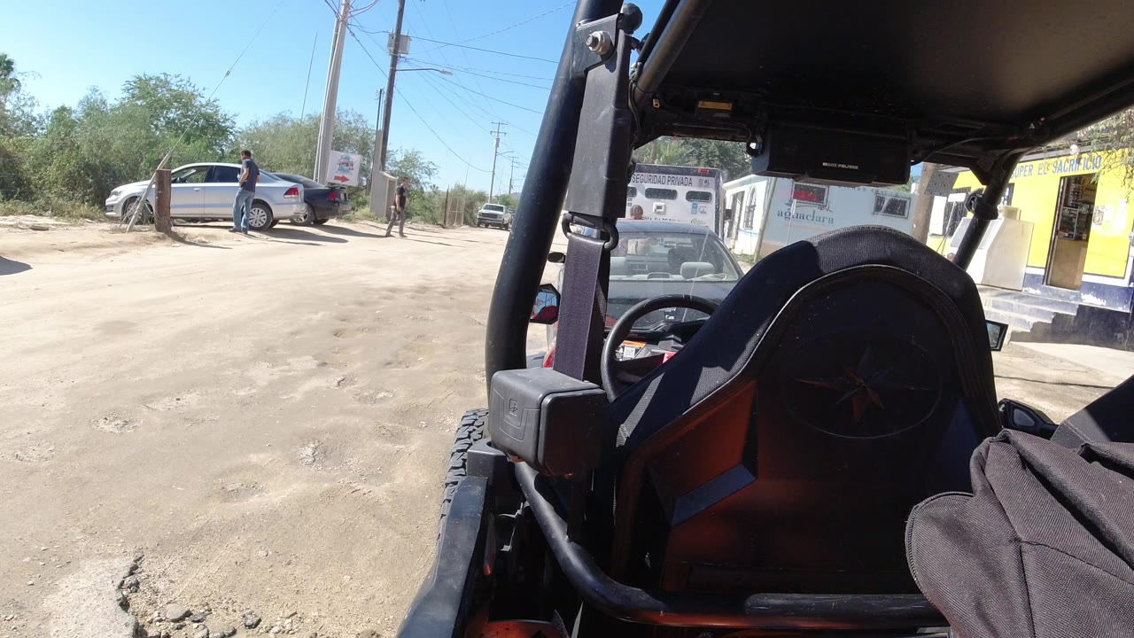 View from a vehicle toward a dusty street with a silver vehicle and people nearby.