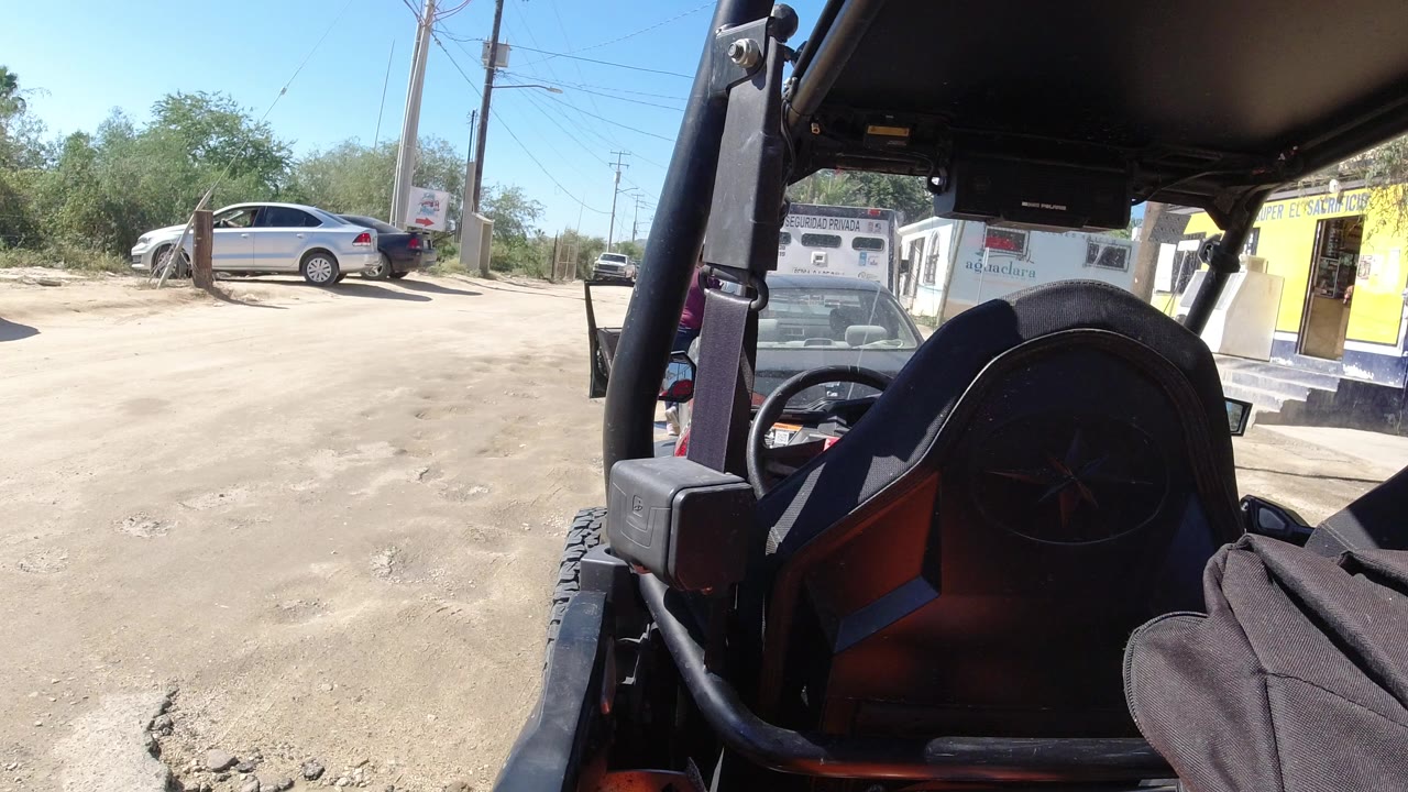 Wrangler interior framing a dusty parking lot outside a yellow storefront.