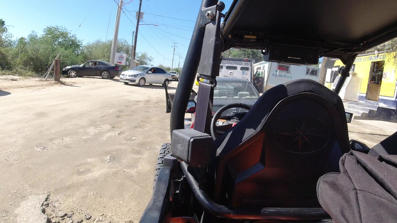 Dusty yard seen past a utility vehicle seat and roll bar.
