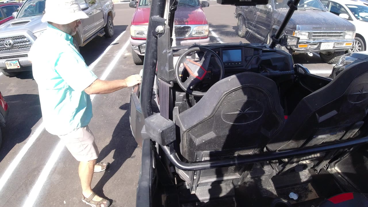 Person in a white hat standing beside an open black vehicle in a parking lot.
