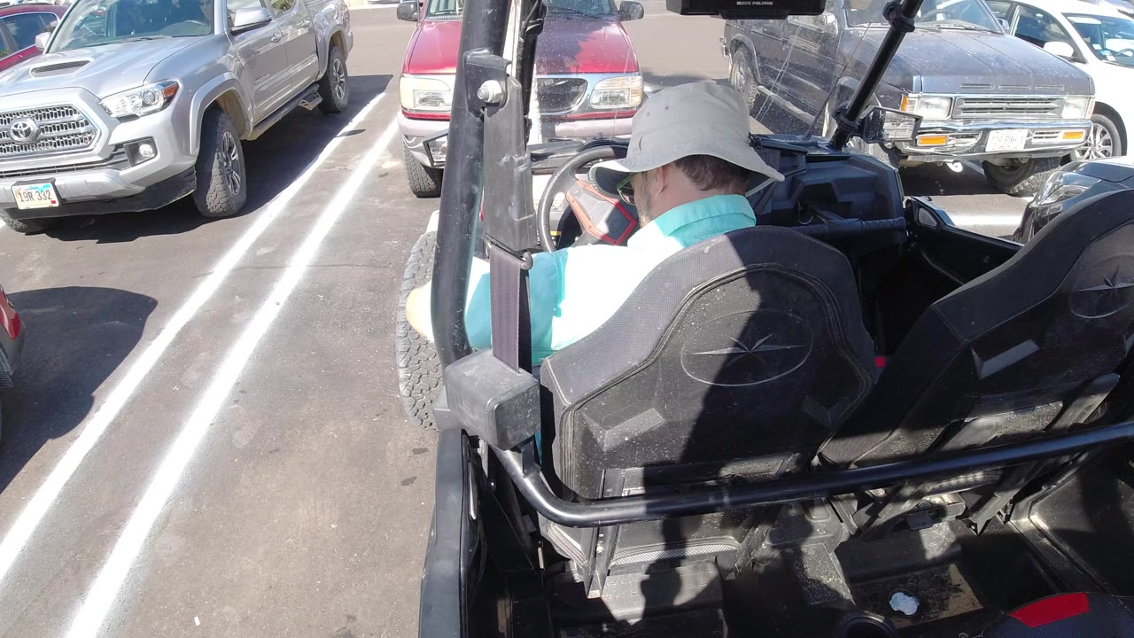 At the start of the Los Cabos clip, a man in a light sun hat sits in an open black vehicle with parked cars and white parking lines ahead.