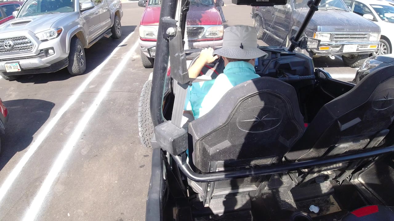 At the start of the Los Cabos clip, a man in a pale bucket hat sits in an open black vehicle between parked cars under bright sun.