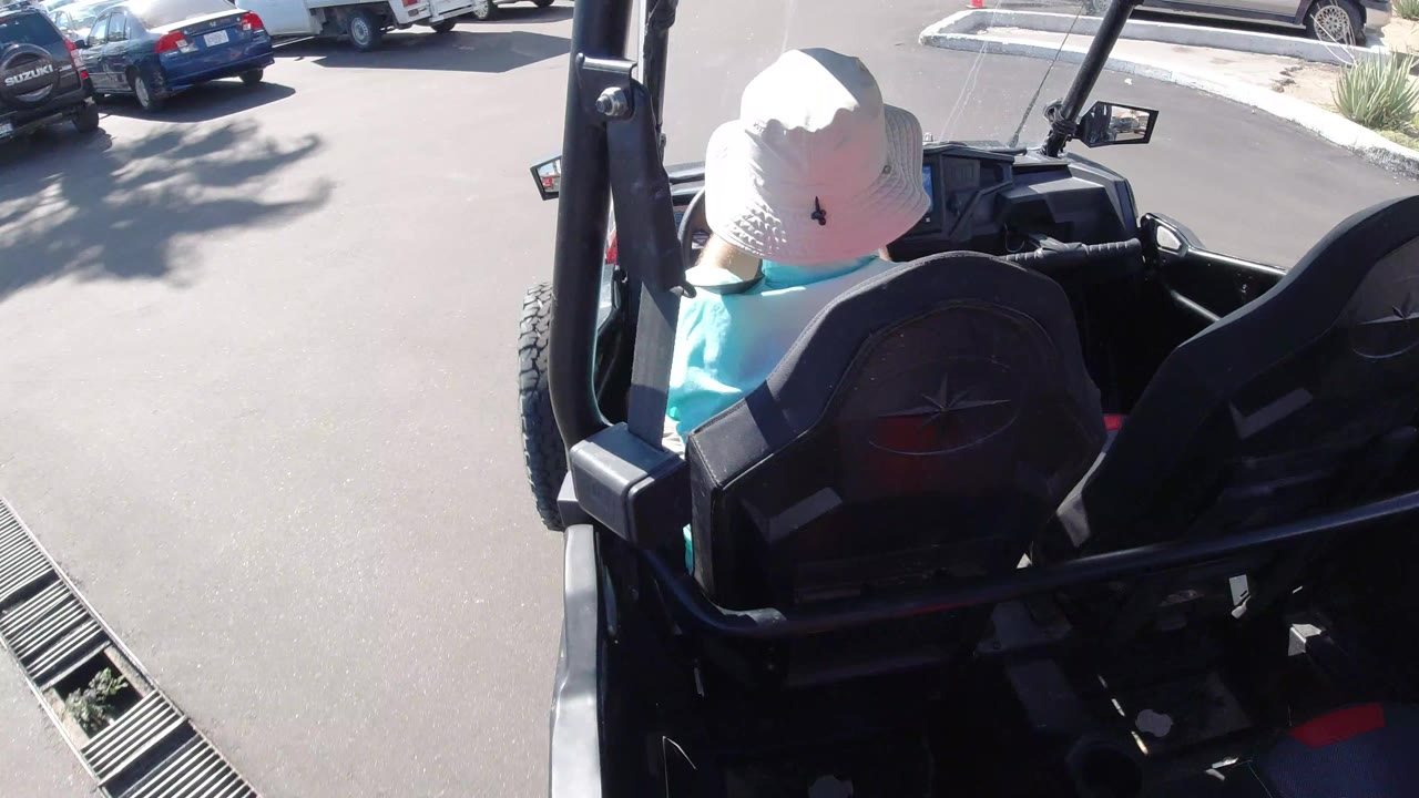 Rear view of a seated passenger in an open vehicle near parked cars.