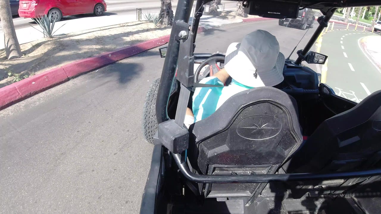 Driver in an open vehicle beside a red curb on a sunny road.