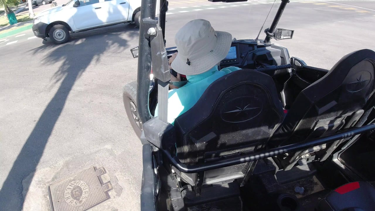 Person in a white bucket hat driving a golf cart near a white pickup truck.