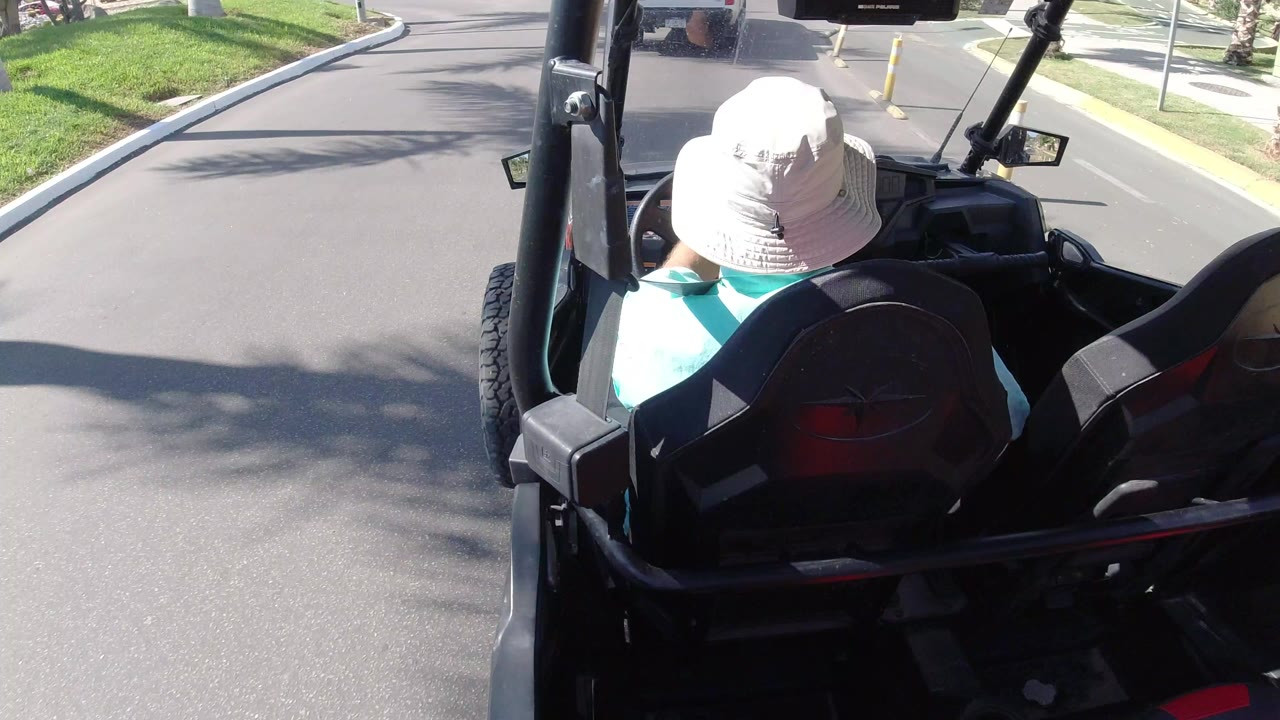 Person in a white bucket hat riding in an open vehicle on a paved road.