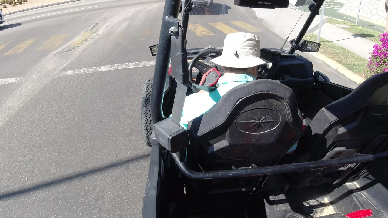 Driver in a white hat seated in an open vehicle at a road intersection.