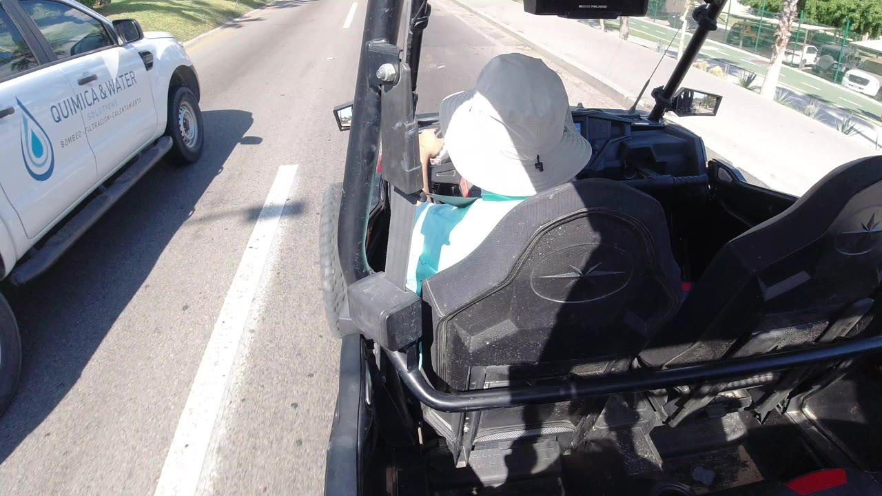 Rear view over the open vehicle in Los Cabos, Mexico with the hat-wearing driver centered and a white pickup truck ahead in the lane.