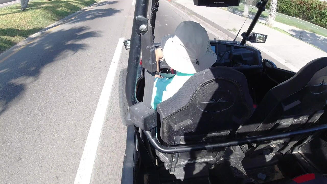 Person in a white hat driving an open black vehicle on a sunny road.