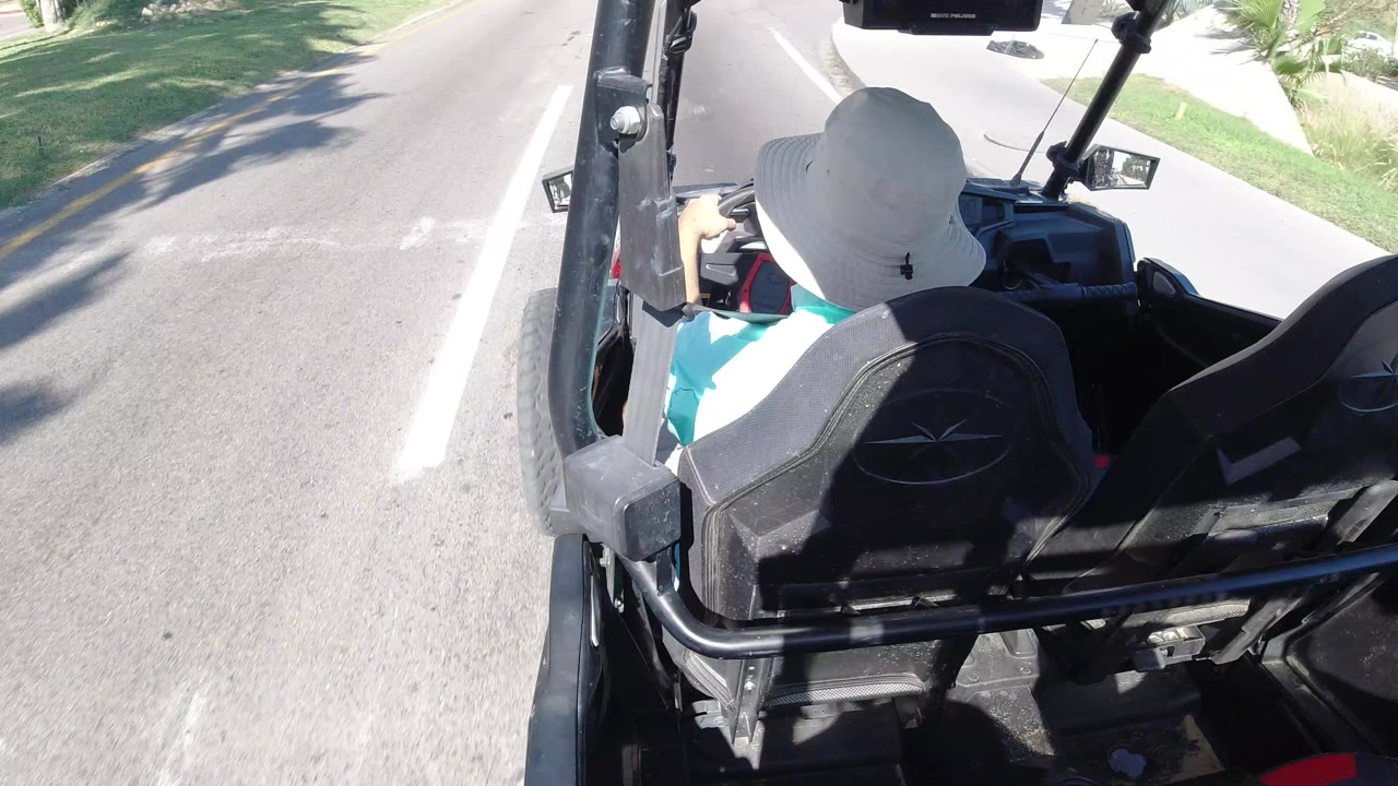 Back of a person in a white hat riding in an open buggy on a paved road.