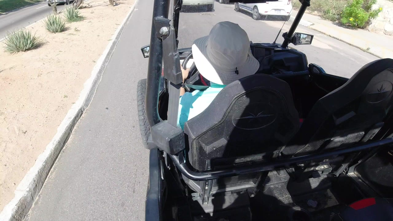 Rear view of a man driving an open black vehicle along a paved road.