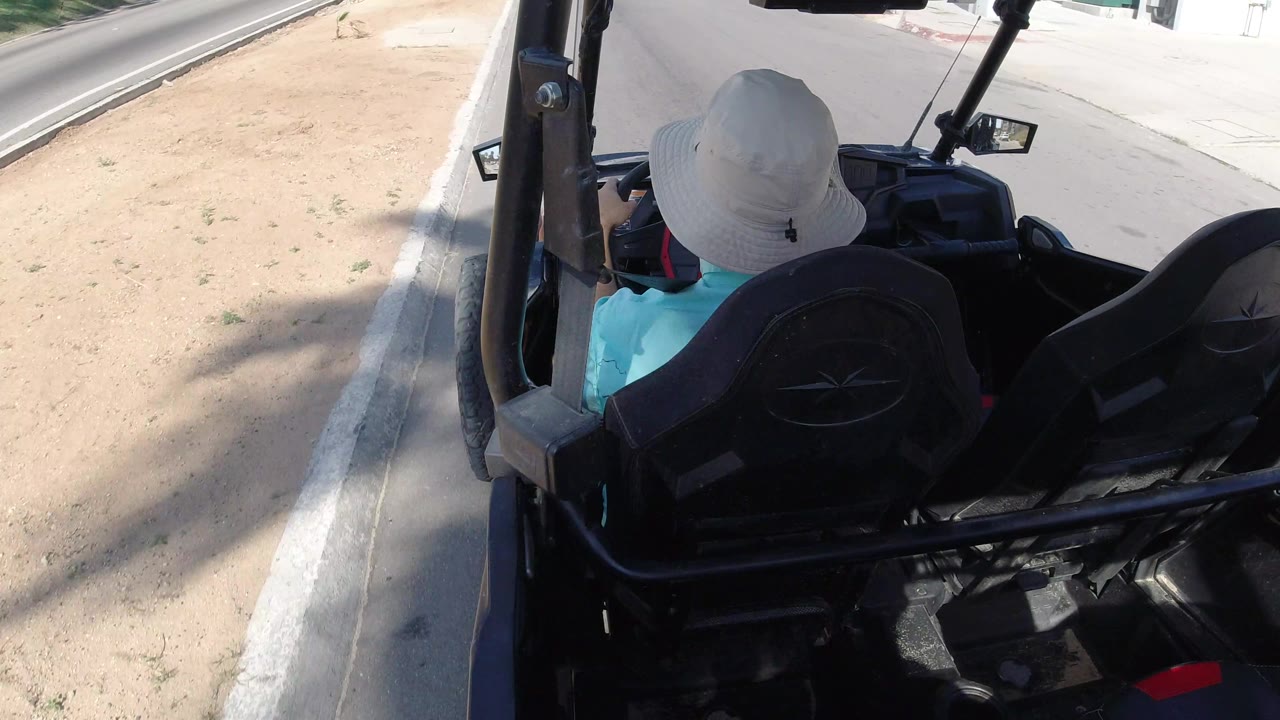 Open vehicle moving past a shaded curb and sandy shoulder.