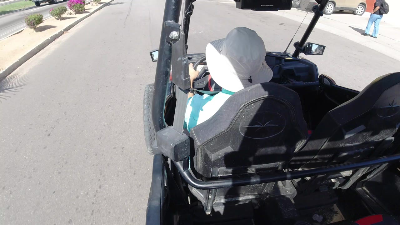 Driver in a white hat seated in an open vehicle on a sunny road.