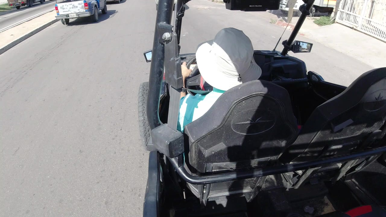 Rear overhead view of a man in a white hat driving an open black vehicle on a paved street.