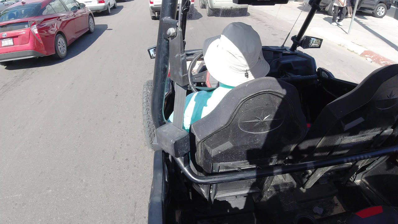 Overhead view into a black golf cart beside cars on a paved street.