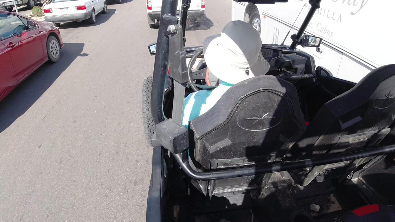 Rear view of a hat-wearing driver in a small open vehicle on a sunny street.
