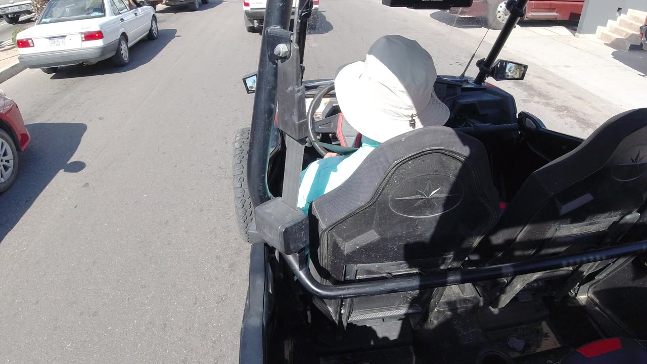 Rear view of a person in a white hat riding in a black open Jeep on a sunny road.