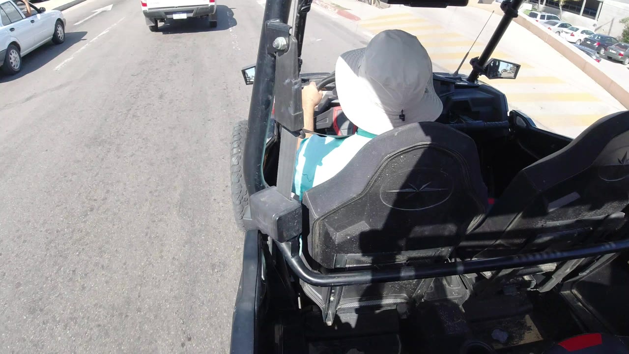 Open vehicle behind a driver in traffic on a sunlit road.
