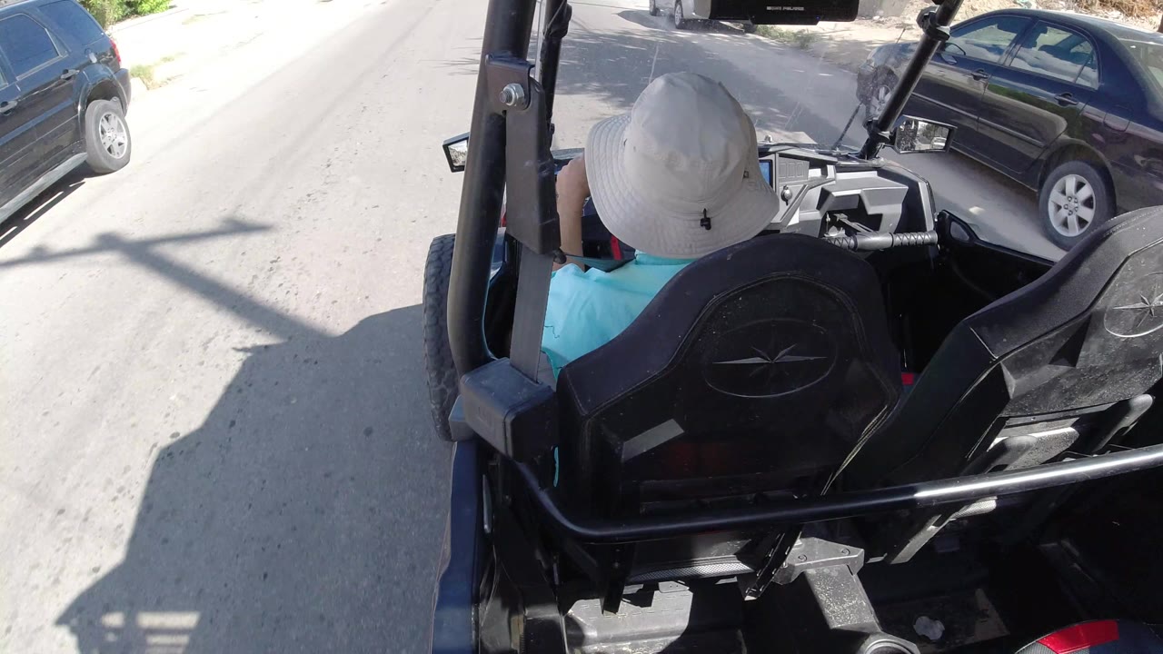 One second in, the driver remains centered in the open vehicle while a dark parked car and bright pavement fill the Los Cabos street view ahead.