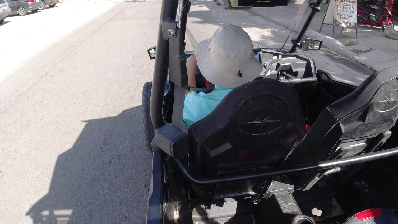 Open vehicle on a bright street near parked cars and scooters.