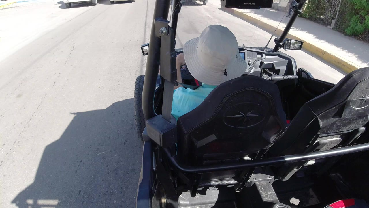 Rear view from an open vehicle on a bright Los Cabos road, with black seats and roll bars in the foreground and no close visible faces.