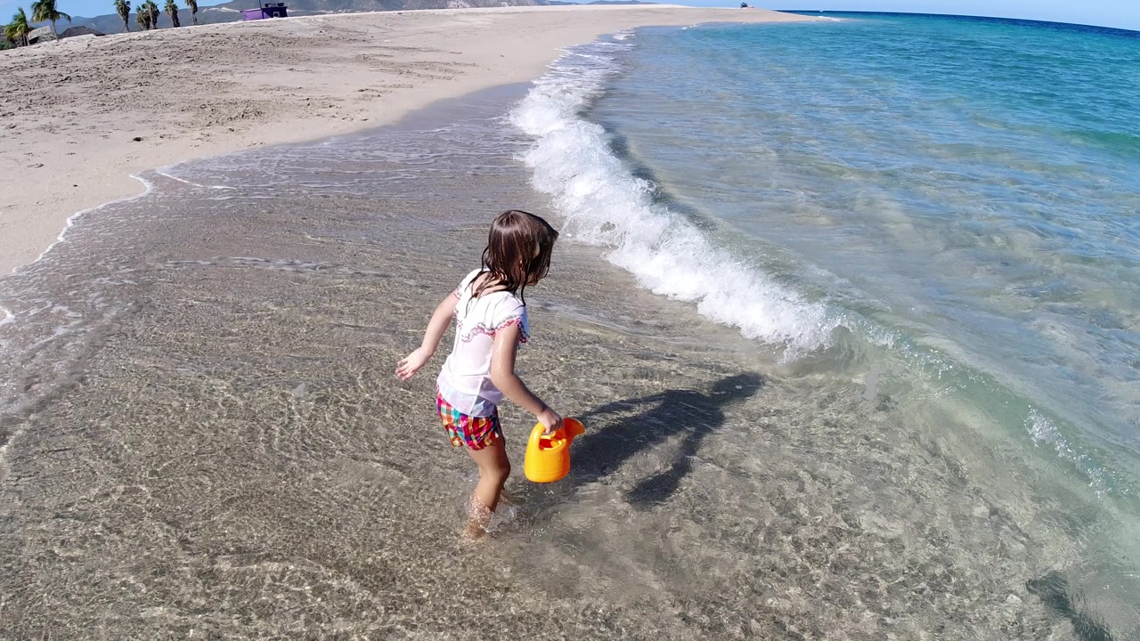 Young girl holding a yellow toy in shallow beach water