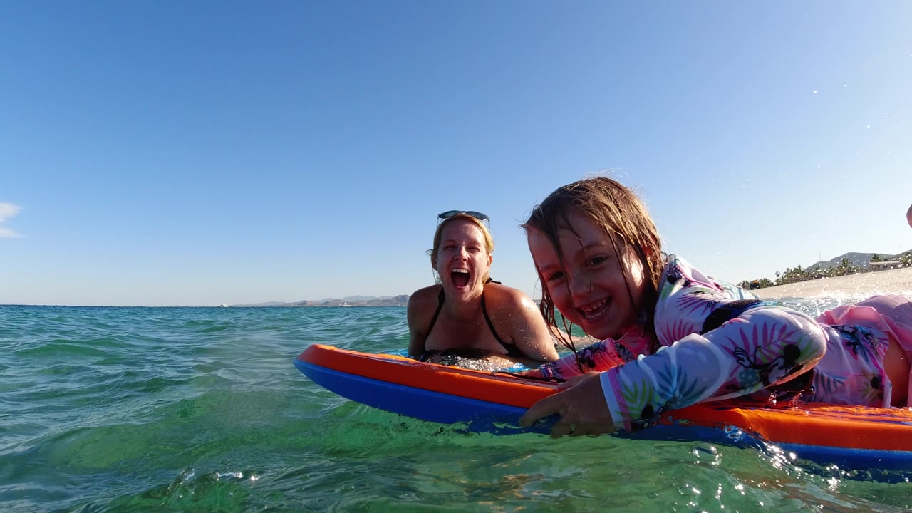 Mother and daughter smiling on bodyboards in the ocean