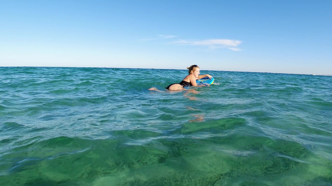 Woman lying on a small board across the ocean surface.