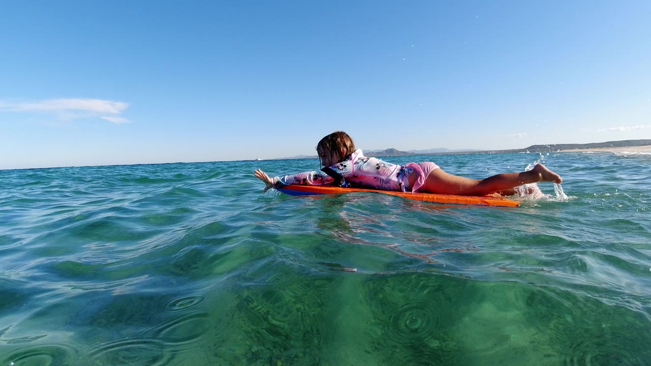 Girl lying on an orange bodyboard in clear ocean water.