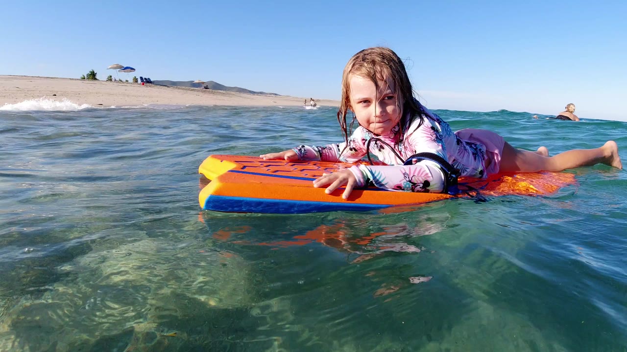 Child lying on an orange bodyboard in shallow beach water.