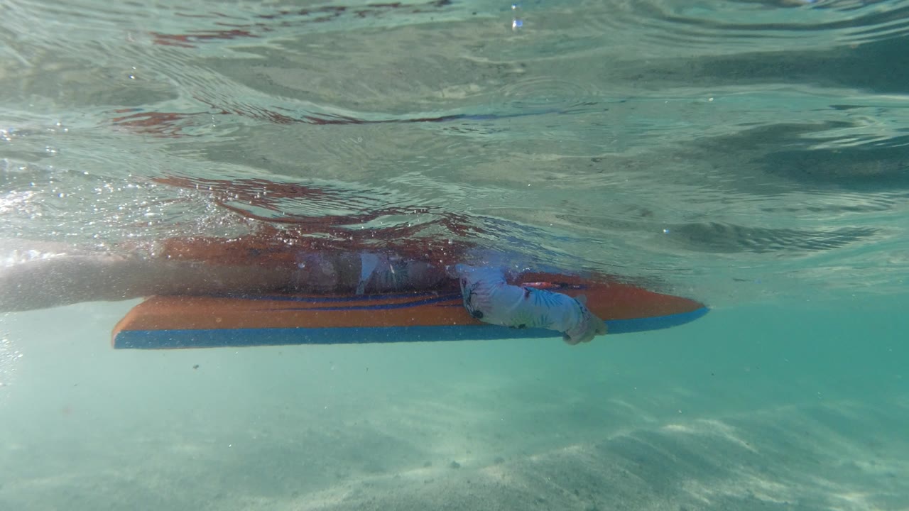 Child underwater beside an orange and blue float in clear water.