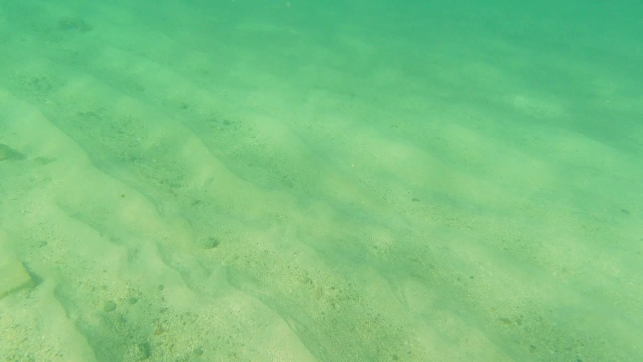 Clear shallow water in Los Cabos, Mexico reveals pale sand ridges and darker stream-like channels, with no visible people.