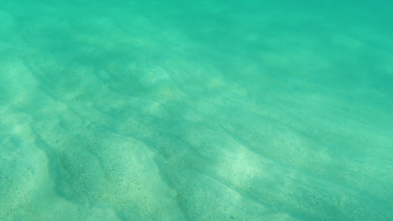 Overhead view of turquoise seawater and pale sand texture in Los Cabos, Mexico, with soft sunlight patterns and no visible people.